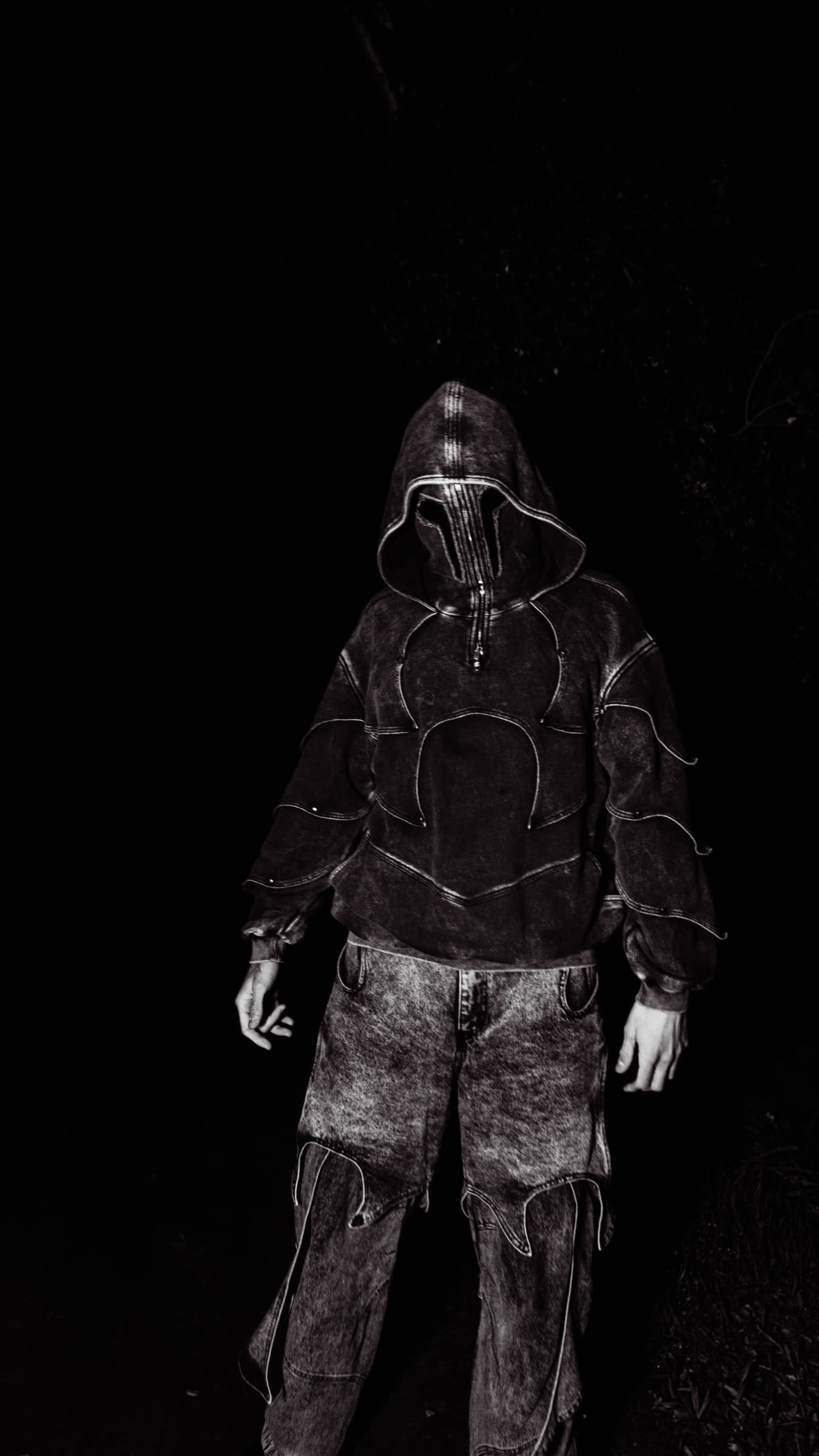 DRACU standing in darkness, hooded and masked, lit from above
